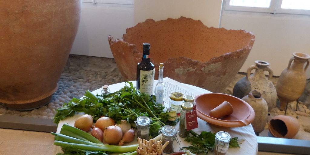 Valence-musée-les-causeries-culinaires-recette-fait-maison-boutique-saveur-histoire Photo de la table avec des produits de consommation de l'époque romaine, en arrière plan des amphores et des délia d'époque.