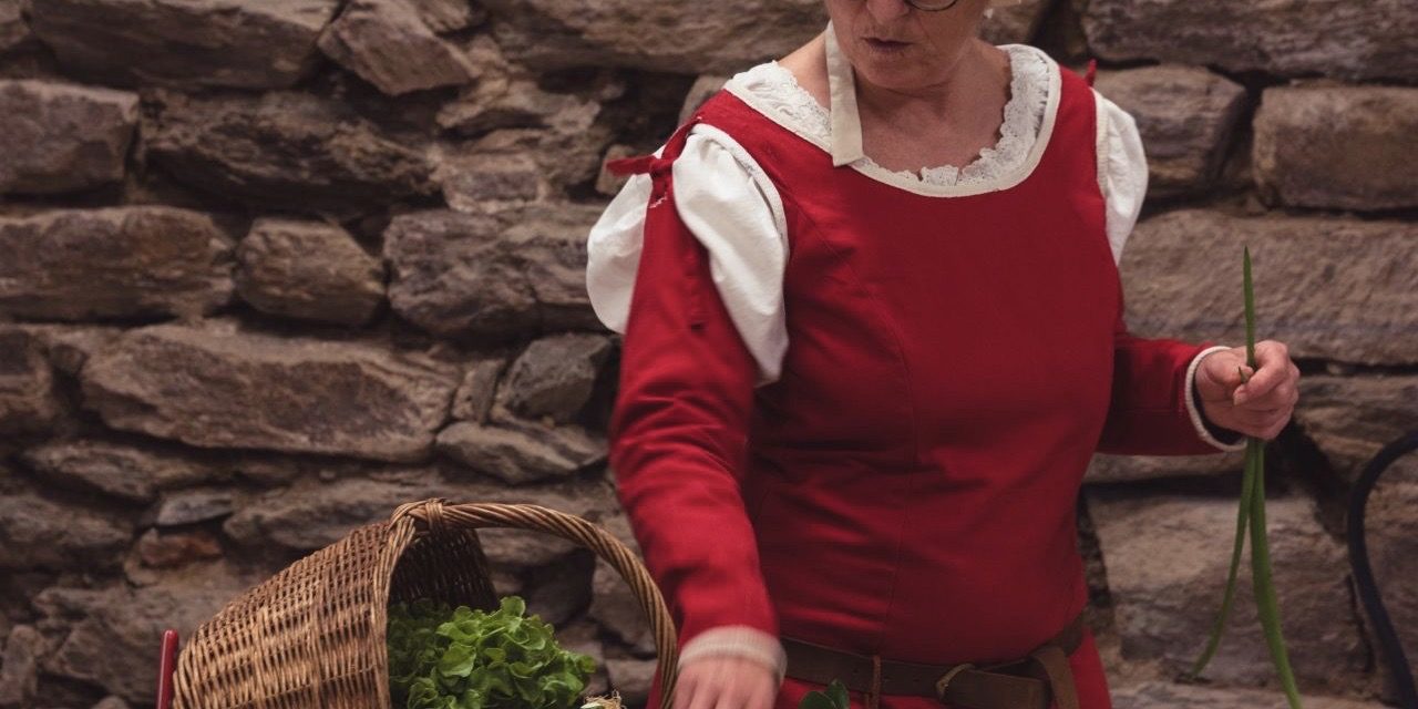 Najac-animation©maisondugouverneurdeNajac photo de l'animatrice costumée présentant le panier de légume de la cuisinière du Moyen Âge