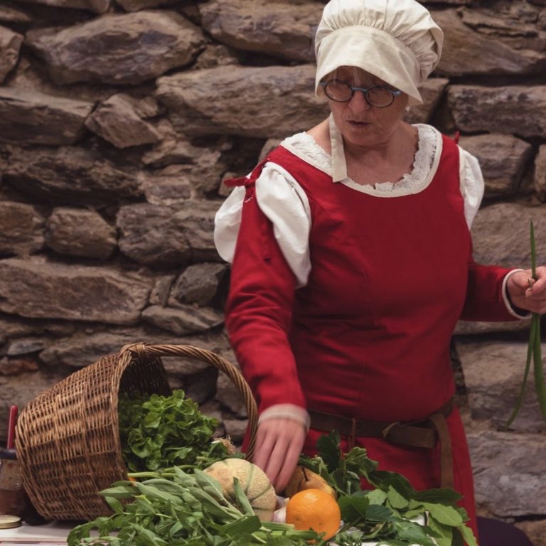 Najac-animation©maisondugouverneurdeNajac photo de l'animatrice costumée présentant le panier de légume de la cuisinière du Moyen Âge